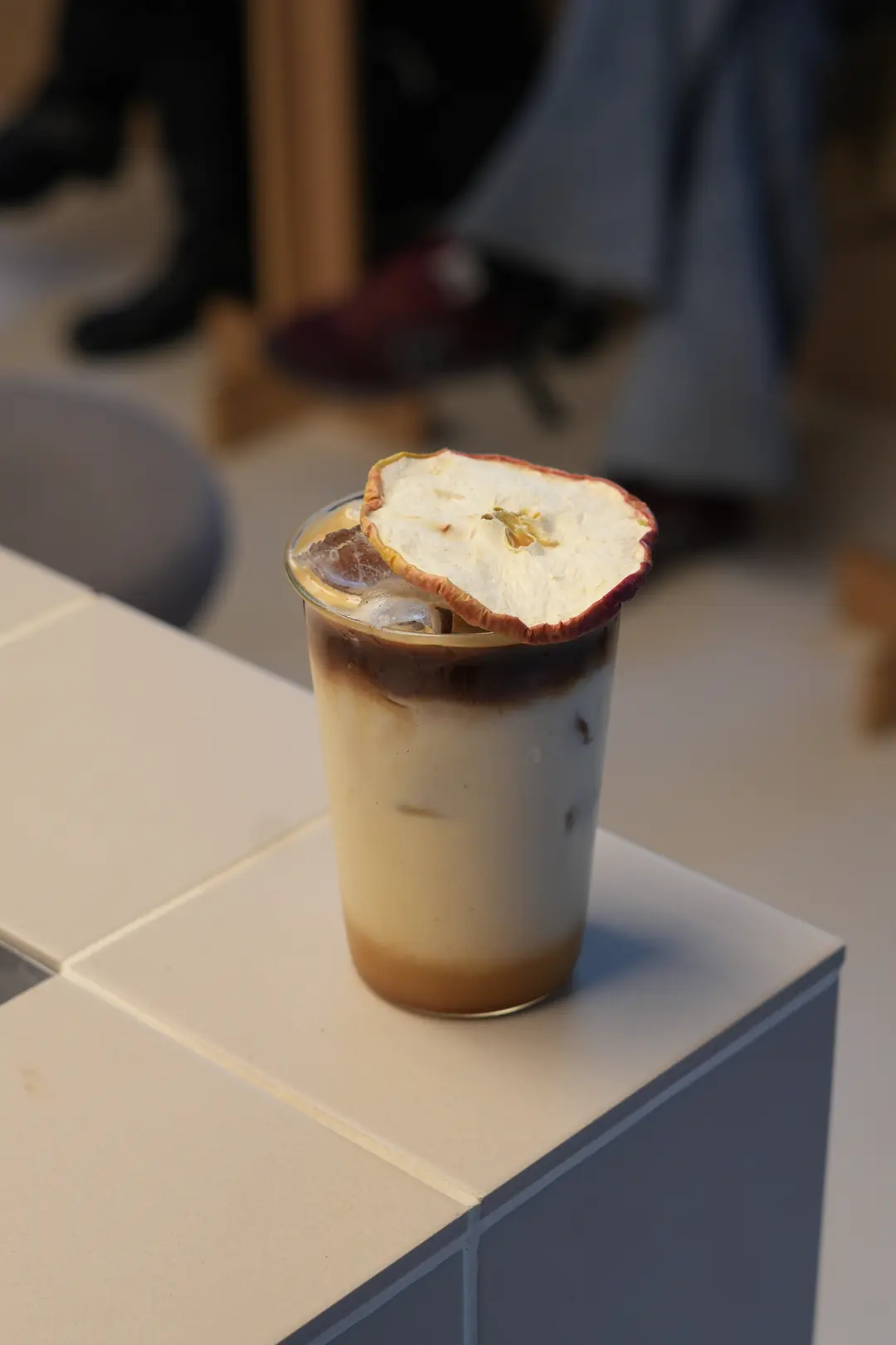 Iced Apple Pie Latte w COPPIE: wysoka szklanka z mlekiem i espresso na lodzie, na wierzchu suszony plaster jabłka