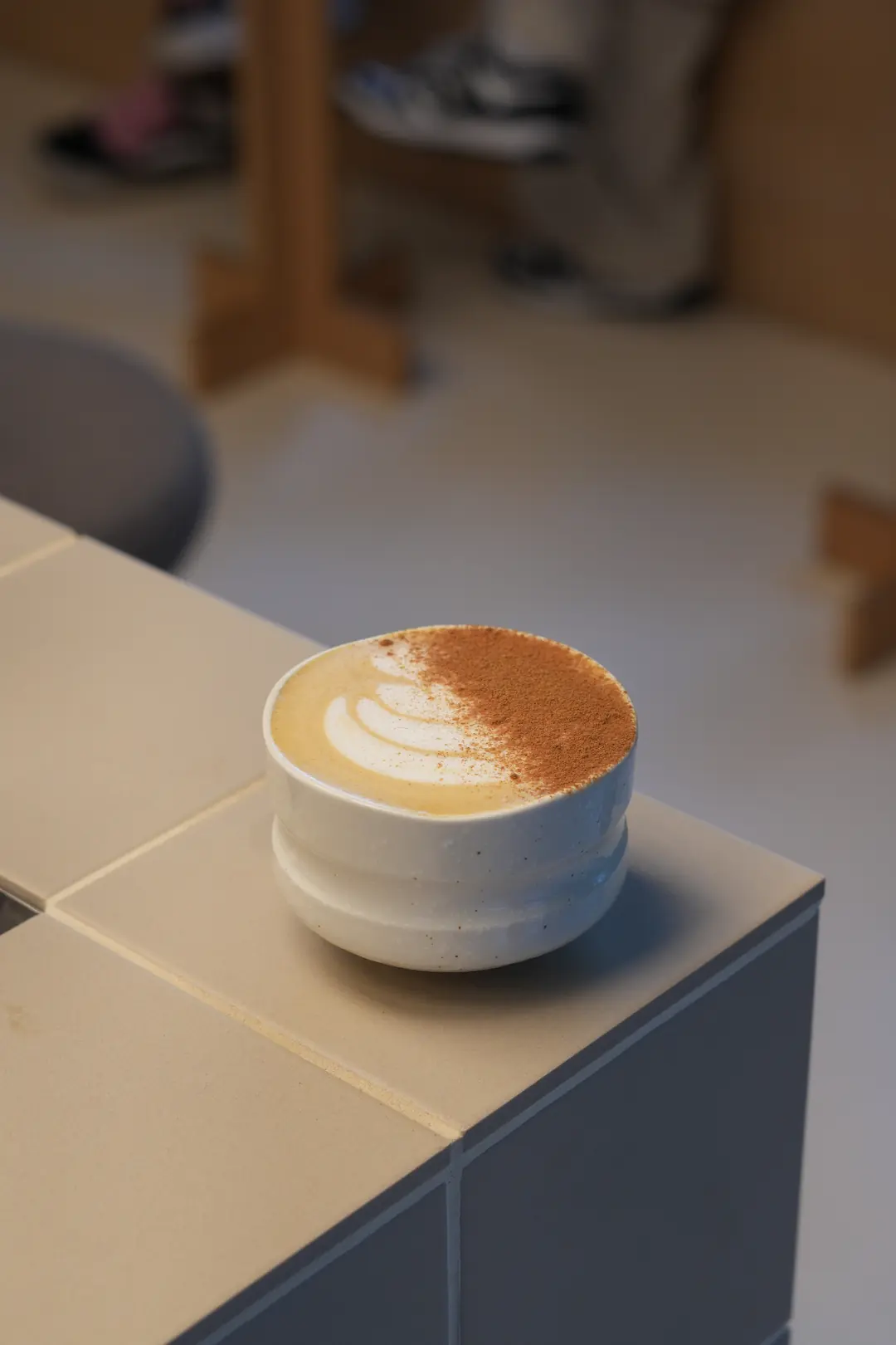 Pumpkin Spice w COPPIE w Krakowie: latte z liściem z mlecznej pianki, w połowie posypane cynamonem, w białej ceramicznej czarce na jasnym kafelkowym barze